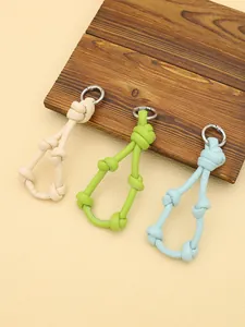 Detailed view of three knotted leather keychain charms in pastel colors on wood.