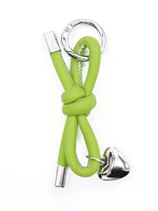 Close-up detail of a minimalist lime green leather knot keychain with heart pendant charm