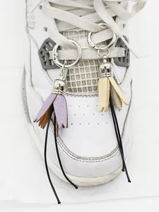 Close-up of handmade PU leather tassel shoe charms in purple and beige on white sneaker