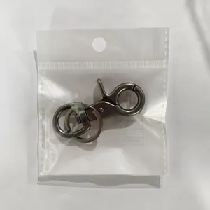 Close-up van een vintage messingkleurige karabijnhaak in zijn transparante plastic zakje.