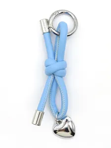 Macro shot of a light blue leather cord knot keychain with a silver heart charm.