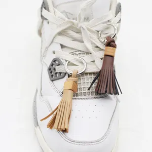 Detail view of handmade PU leather tassel shoe charms attached to a white sneaker lace