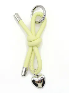 Close-up detail of a handmade yellow leather knot keychain with a silver heart charm