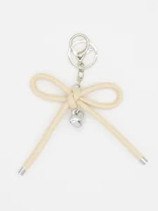 Detailed macro view of minimalist beige leather bow keychain with silver heart charm