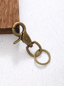 Detailopname van vintage messinglegering karabijnsluiting en sleutelring op wit textuur.