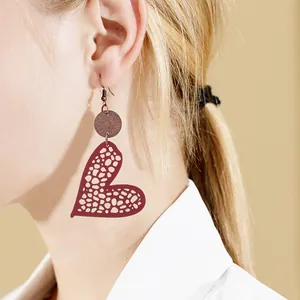 Close-up of heart-shaped cutout leather earrings with wooden disc on model