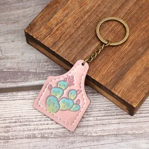 Detail view of a western farm style cactus cattle ear tag keychain on rustic wood background