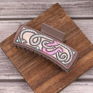Detail van Western cowboy haarklem met roze letter en touwpatroon op houten achtergrond