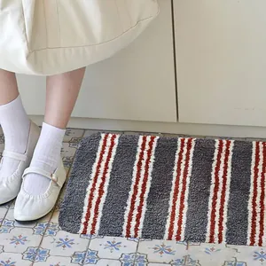 Detail van een zachte badmat met grijze en rode strepen op een gedecoreerde tegelvloer