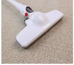 Close-up of white vacuum brush head cleaning a beige textured carpet mat