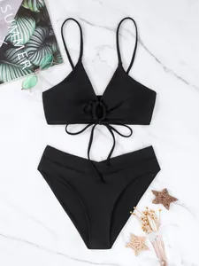 Dettaglio di un bikini nero a due pezzi con lacci su uno sfondo di marmo bianco pulito