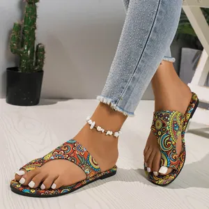 Detailopname van etnische platte sandalen met paisley-prints op een houten vloer