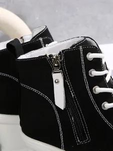 Close-up of side zipper and contrast stitching on black high-top canvas sneakers.