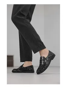 Side detail view of black pleated leather loafers paired with formal grey trousers