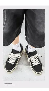 Top-down view of black canvas sneakers with cream sole and wide white laces on ground