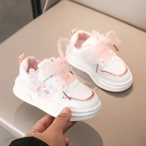 Dettaglio di sneakers bianche da bambina con farfalla glitterata e lacci in nastro rosa