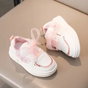 Primo piano di sneaker bianche da bambina con fiocco in organza rosa e dettaglio a farfalla
