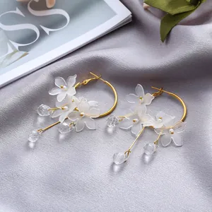 Close-up of elegant gold hoop earrings with white frosted flower petals and crystal tassels.