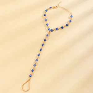 Detailed view of a gold-tone hand harness with blue Evil Eye beads on a beige surface