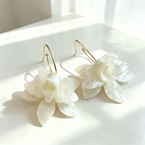 Detailed view of white pearlescent flower petal earrings with elegant gold hooks