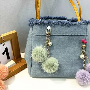 Detalle de un lindo llavero de pompones con perlas colgado de un elegante bolso de mezclilla