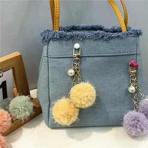Primer plano de un lindo llavero de bola de peluche con perla en un bolso vaquero