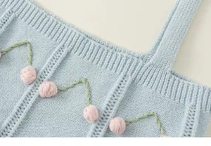 Close-up of light blue knitted girls' vest with cute 3D pink cherry floral embroidery