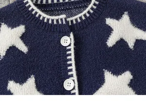 Detail van donkerblauw gebreid kindervest met witte sterpatronen en witte ronde knopen