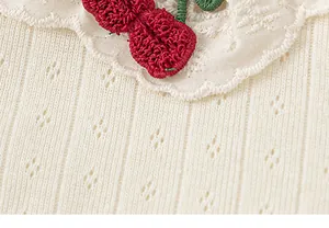Close-up of girl's cream ribbed shirt with lace collar and crochet cherry
