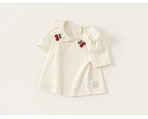 Close-up of cherry embroidery and ruffled collar on a cream textured baby t-shirt.