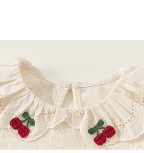 Close-up of girl's cream T-shirt with lace ruffle collar and cherry embroidery