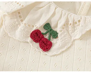 Close-up detail of a baby girl's white t-shirt featuring cherry embroidery and ruffled collar