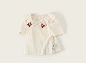 Detail view of girl's cream T-shirt featuring delicate cherry embroidery and lace collar.