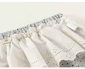 Dettaglio della balza in pizzo ricamato bianco su capo per bambini grigio con stampa stelle