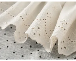 Dettaglio del bordo in pizzo sangallo bianco su tessuto grigio con piccole stelle