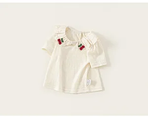 Detailed view of baby girl's cream T-shirt with ruffled collar and cherry embroidery