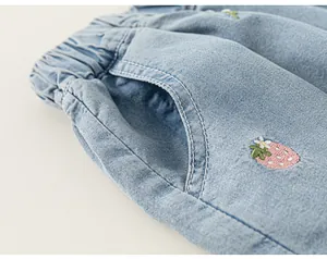 Detailed macro view of girls light blue denim shorts featuring cute strawberry embroidery
