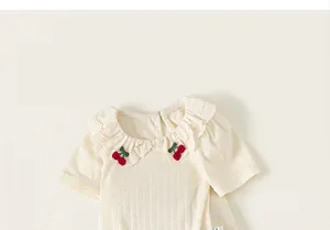 Detail view of girls' off-white pointelle T-shirt with ruffled cherry collar and soft knit fabric
