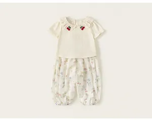 Close-up of girls' ivory ruffle collar t-shirt with cherry detail and floral pants