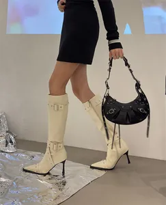 Detail view of cream knee-high stiletto boots with silver studs and buckles