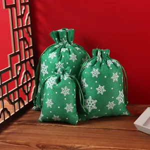 Set of three green burlap-style Christmas drawstring gift bags featuring white snowflake patterns