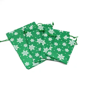 Detail view of green faux linen Christmas bags with white snowflake pattern and drawstrings.