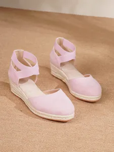 Primer plano de sandalias con cuña tipo alpargata rosa y correas cruzadas de tobillo.