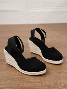 Detalle de sandalias de cuña de lona negra con suela de esparto y correas elásticas