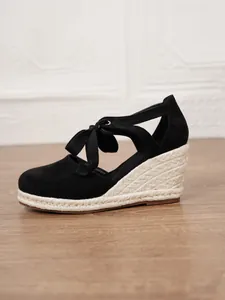 Vista lateral de sandalia de cuña de ante negro con lazo y suela de paja trenzada