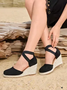 Detalle de sandalias de cuña tipo alpargata negra con tiras al tobillo sobre el modelo.