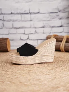 Sandalias de cuña negras con plataforma de paja trenzada sobre un fondo de madera rústico