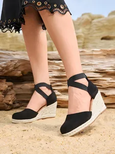 Elegantes sandalias negras de cuña tipo esparto para mujer en un entorno de playa natural.