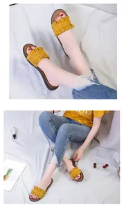 Detailed view of yellow ruffle flat sandals worn with denim jeans on a white backdrop.