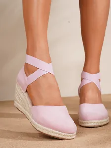 Detalle de sandalias de cuña tipo alpargata rosa con correas cruzadas en el tobillo.